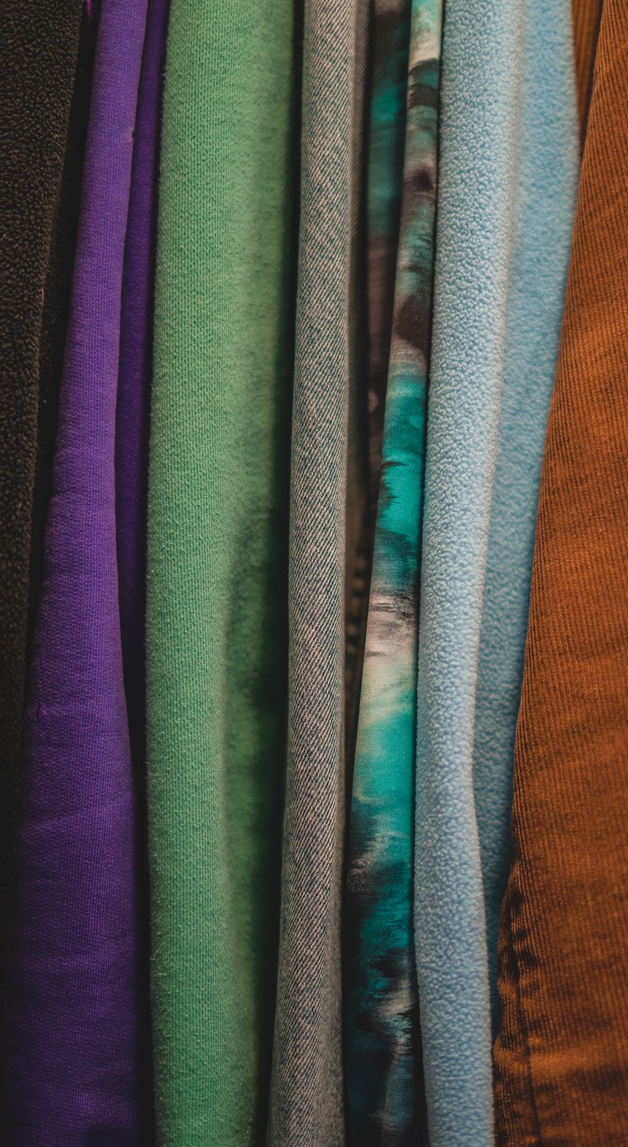 Folded bolts of fabric in purple, green, grey, teal and rust