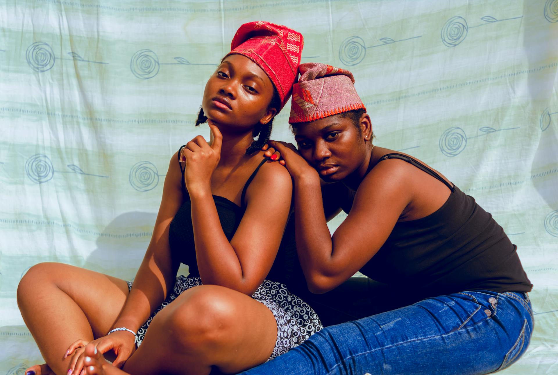 Portrait of two African women in traditional Nigerian attire sitting together indoors.