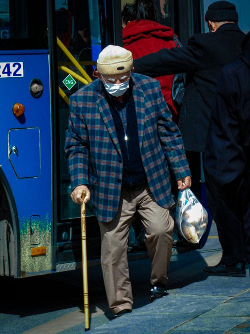 Free Senior man wearing mask exiting bus with walking stick and bag. Stock Photo