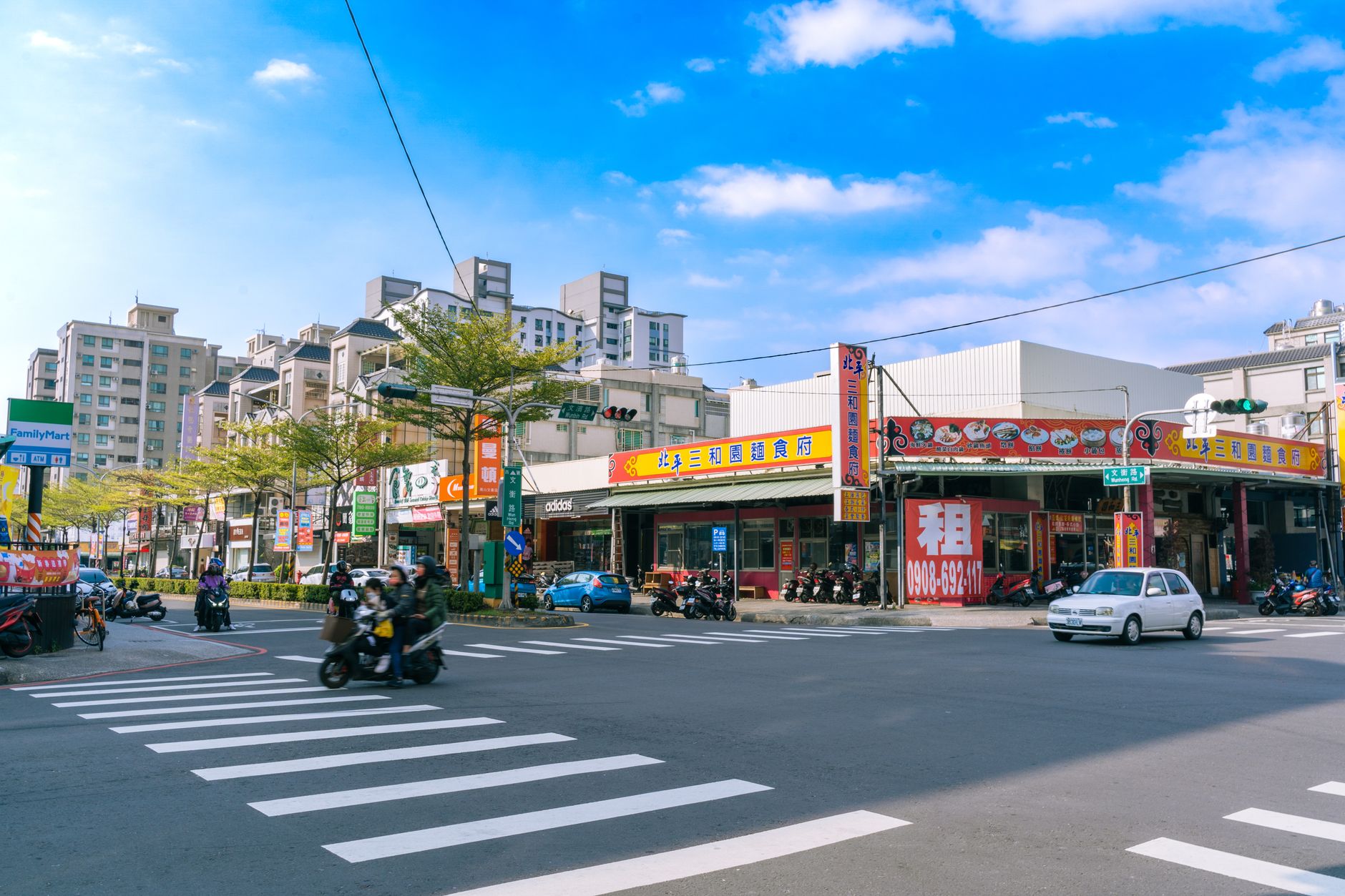 高雄順遊景點規劃:自屏東與台南出發的完整路線與美食攻略 Vibrant street intersection in Kaohsiung, Taiwan with vehicles and pedestrians under a blue sky