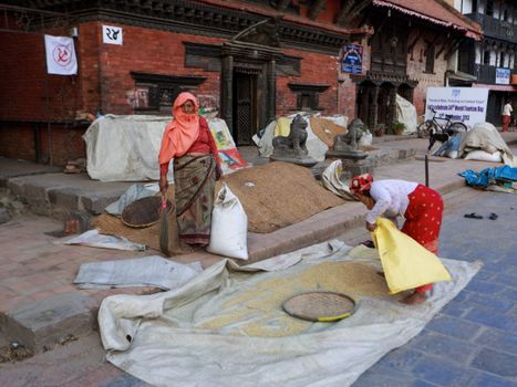 Women sorting grains on the street in a historic city setting. Cultural and everyday life scene.
