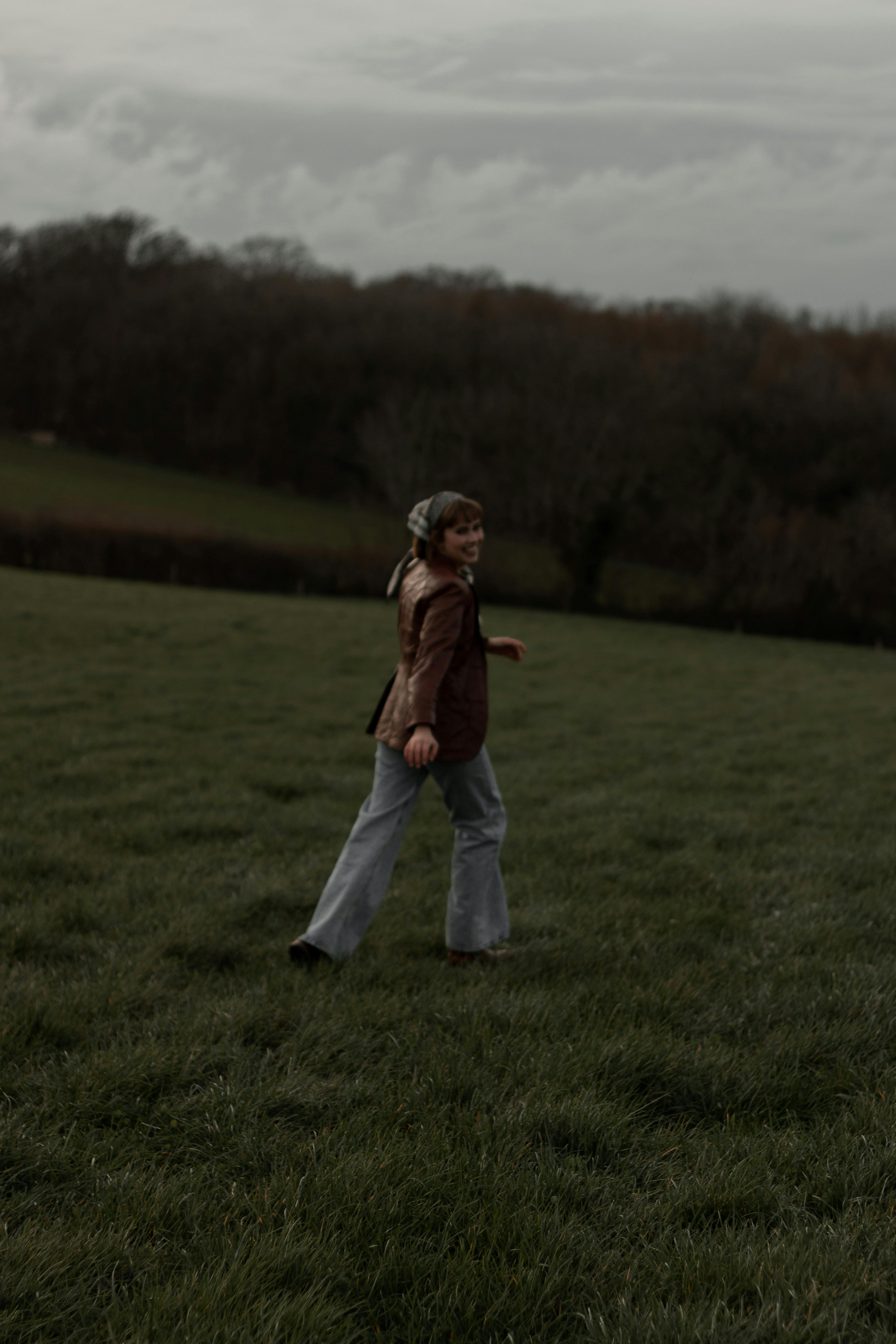 Woman in Brown Jacket Walking on Grass Field · Free Stock Photo