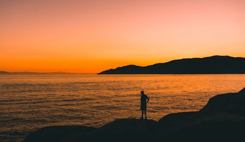 Silhouette of a Man Standing on Mountain Top Beside the Sea