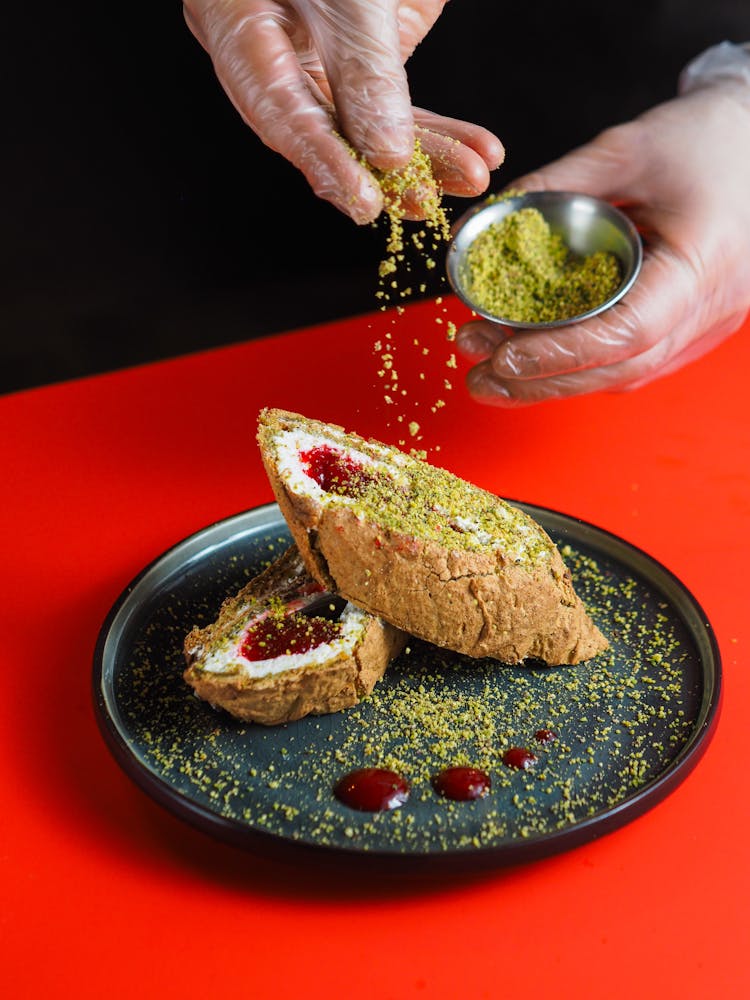 Person Sprinkling Pistachio Powder On A Dessert