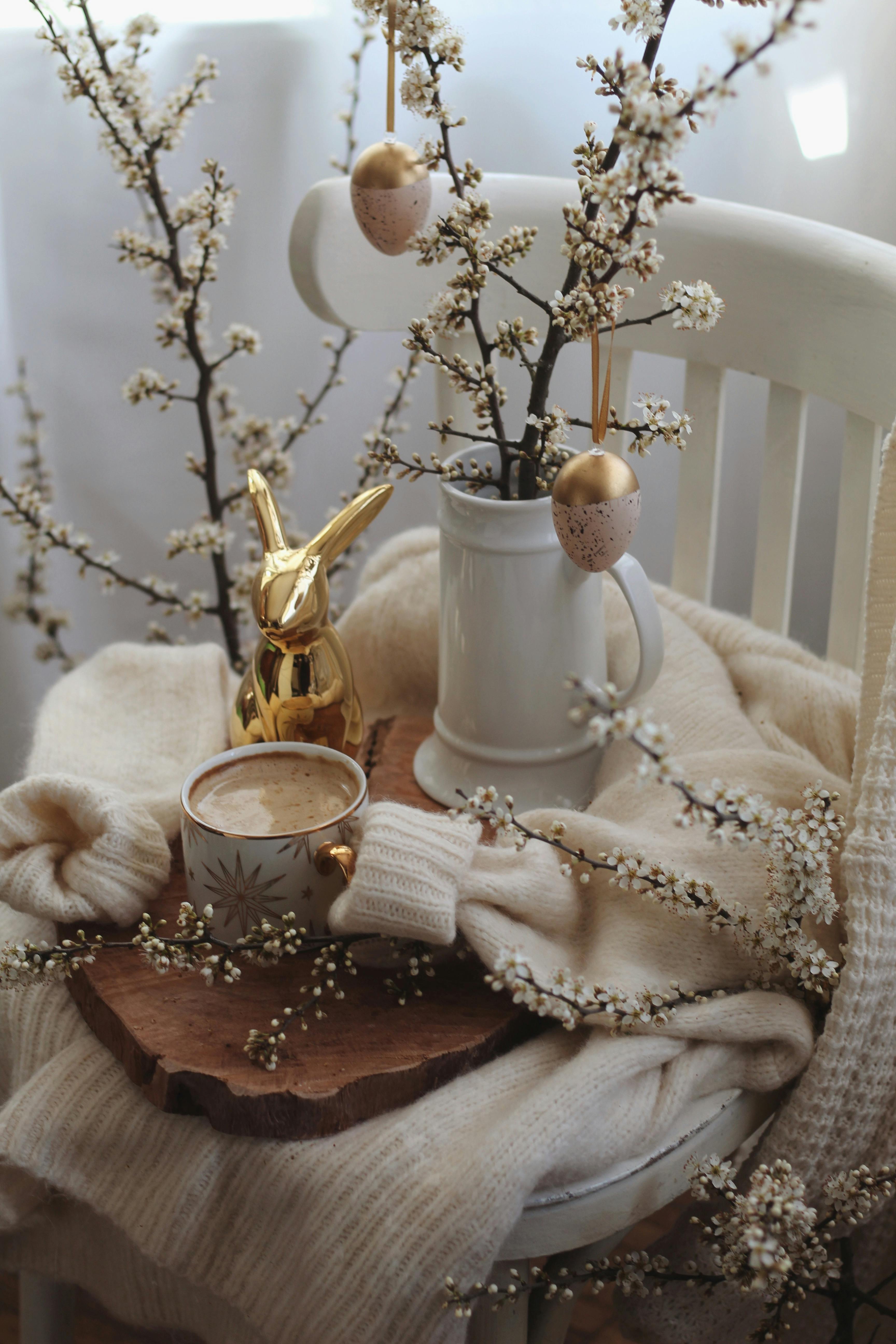 Charming still life of coffee, delicate blossoms, and cozy decor in a warm setting.