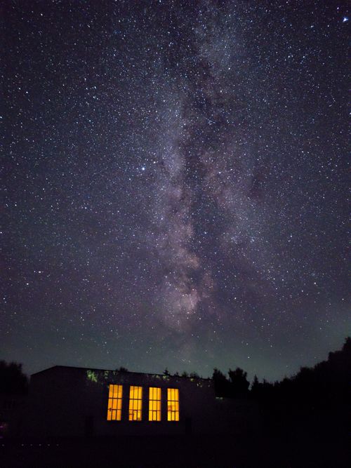 Free A stunning view of the Milky Way stretching across the night sky above a lit building. Stock Photo