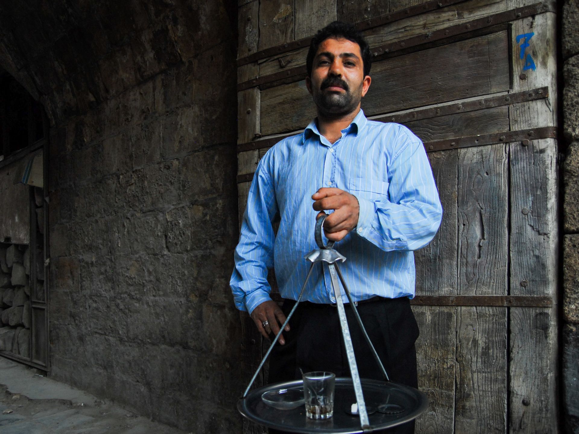 Middle-aged bearded man serves coffee in a rustic street setting, showcasing traditional culture.