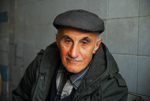 Free Close-up portrait of an elderly man wearing a flat cap indoors, exhibiting wisdom and warmth. Stock Photo