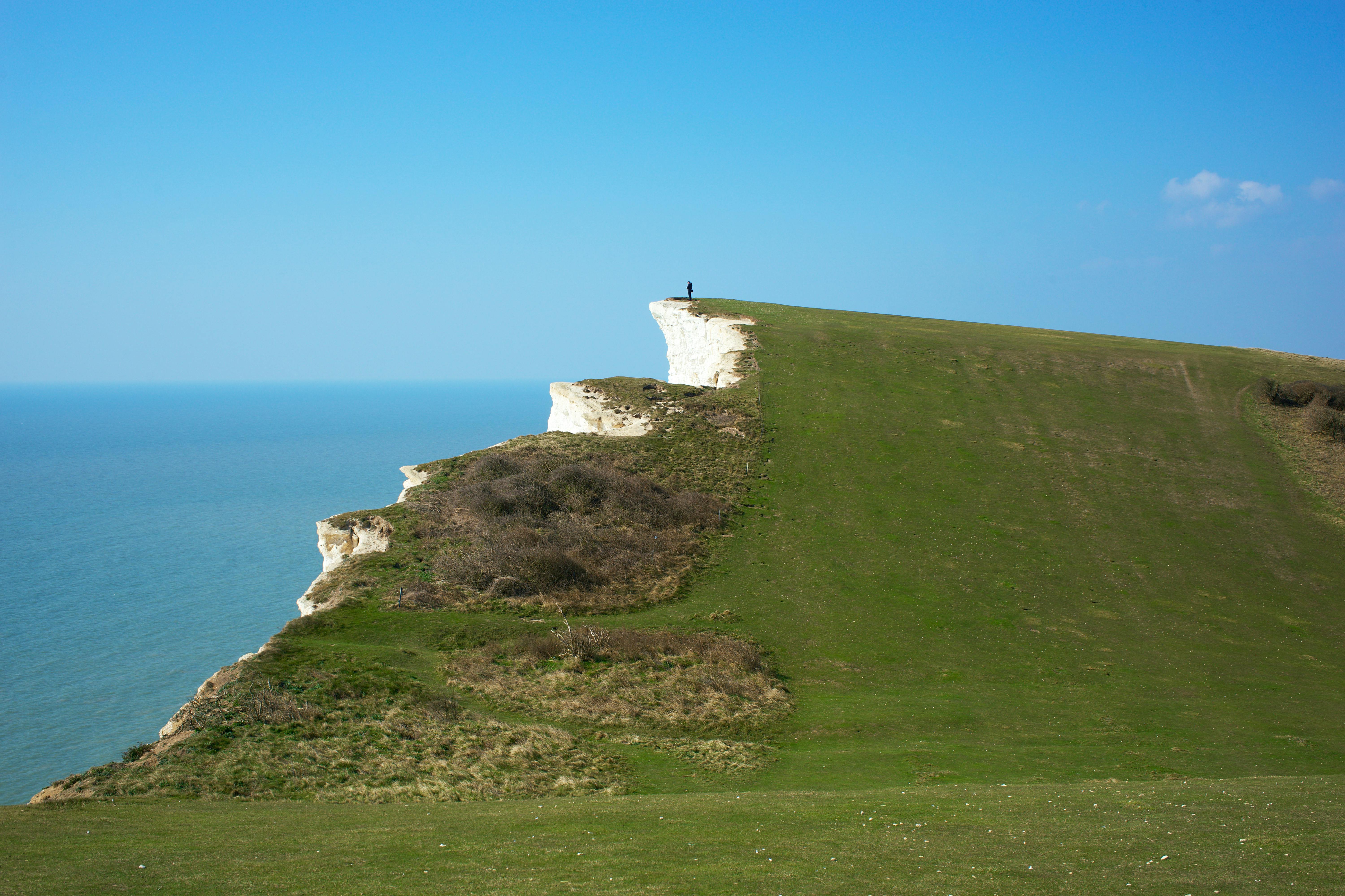 Solitary figure standing on the majestic chalk cliffs of Beachy Head, overlooking the sea in East Sussex, England.