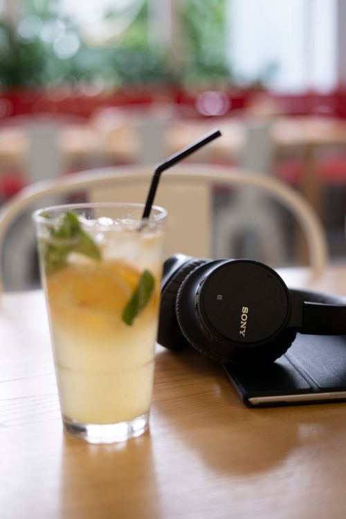 Free A glass of lemonade with mint leaves beside stylish headphones on a wooden table in a cafe setting. Stock Photo