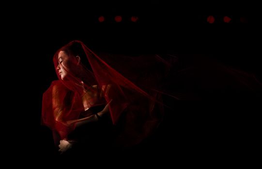 Artistic portrait of a woman draped in a red veil set against a dark studio background.