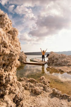 A woman raises her arms in celebration by the rocky shore, reflecting freedom and travel.