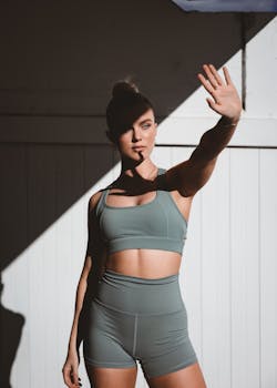 Portrait of a woman in gym wear outdoors, shielding face with hand under sunlight.