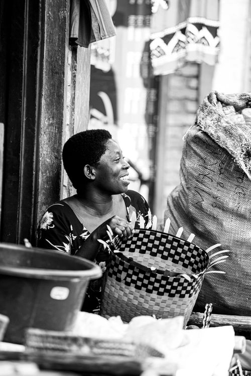 Free Black-and-white photo of an African woman smiling with a woven basket in a market setting. Stock Photo