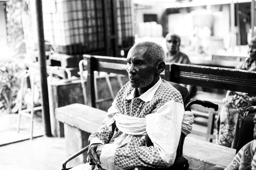 Monochrome image of an elderly African man sitting in a wheelchair outdoors, conveying resilience.