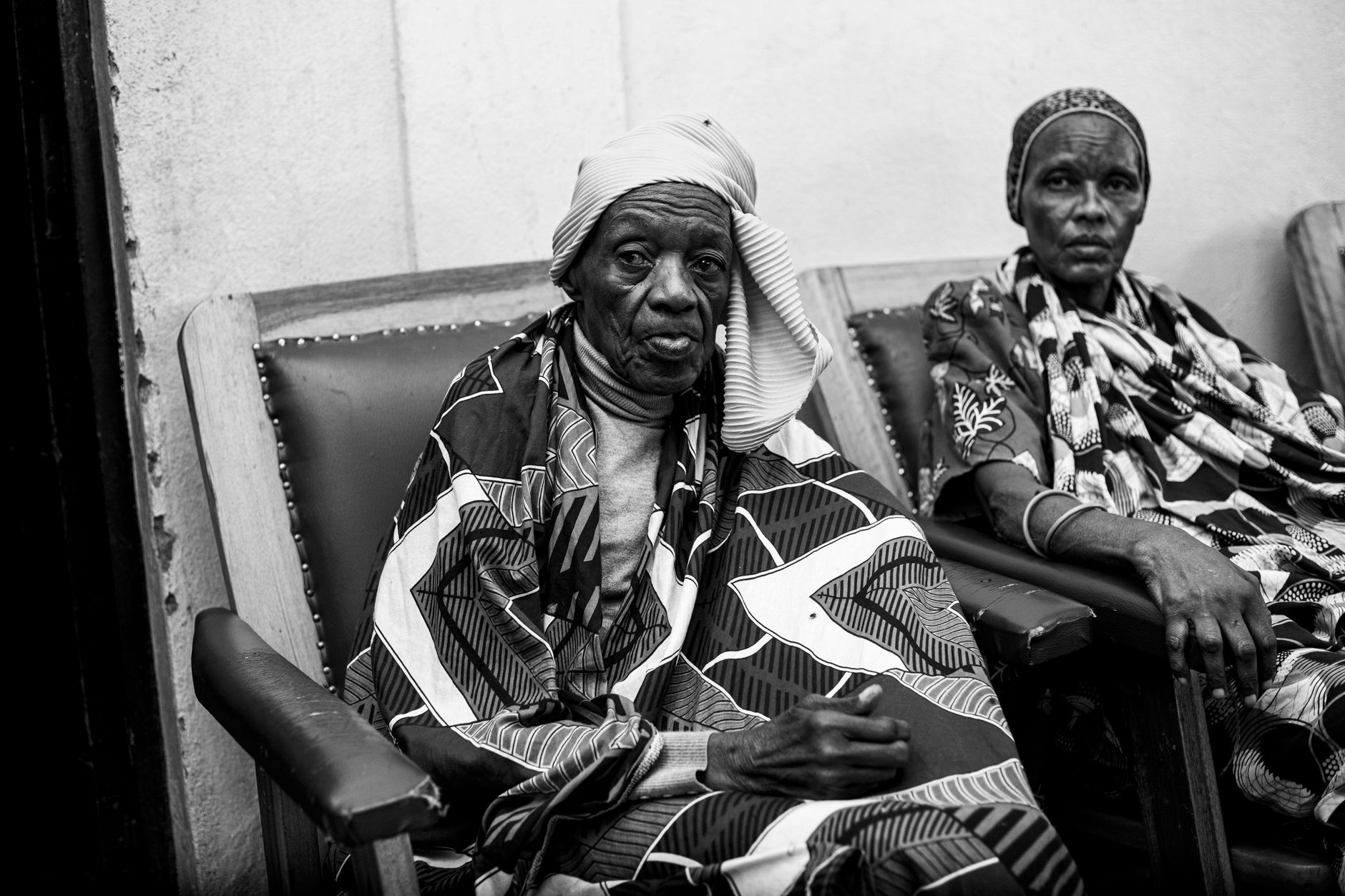 Black and white photo of elderly women in traditional African garments sitting in chairs.