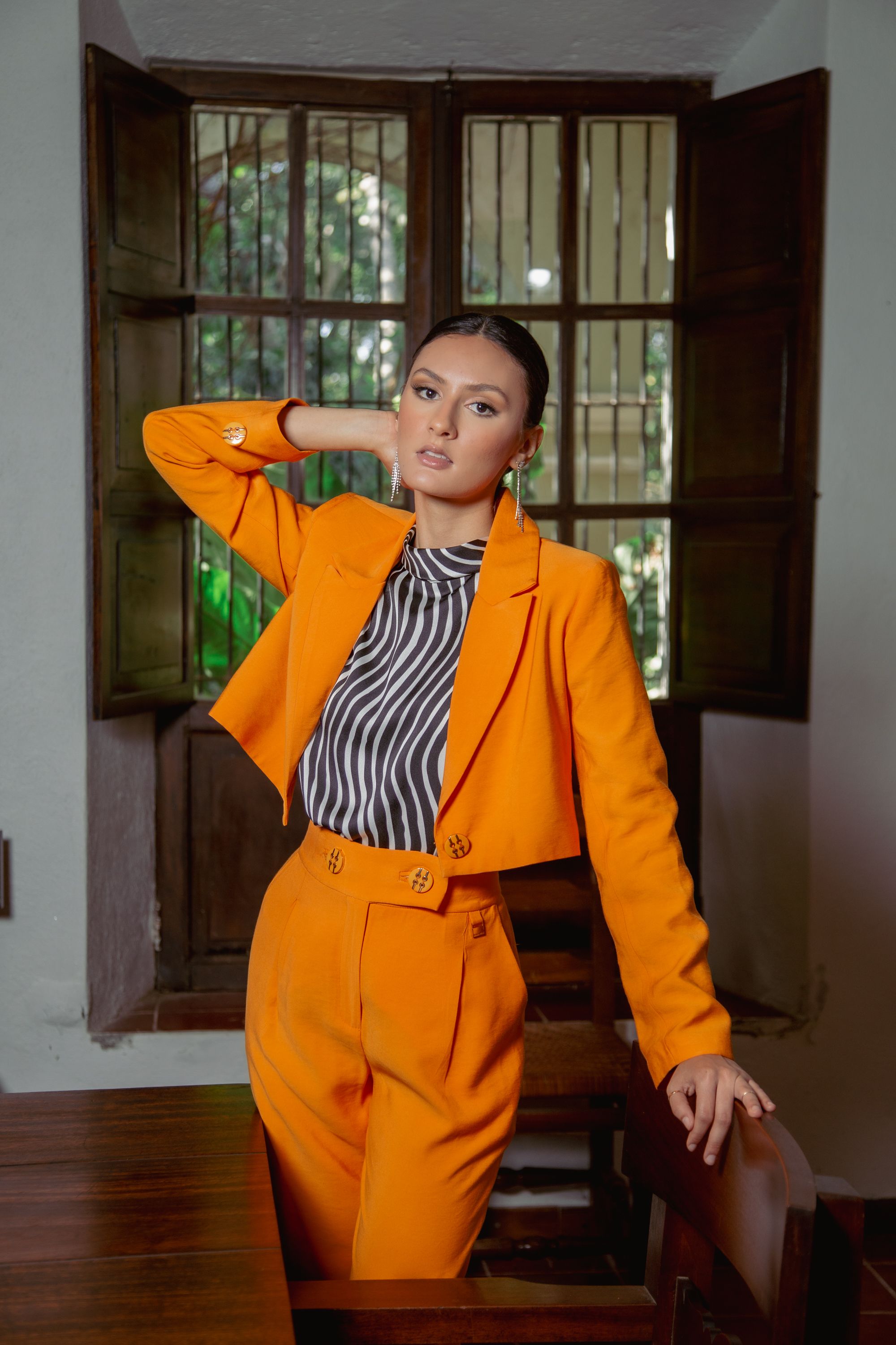Mulher confiante em um vibrante conjunto laranja dentro de casa, exibindo moda moderna.