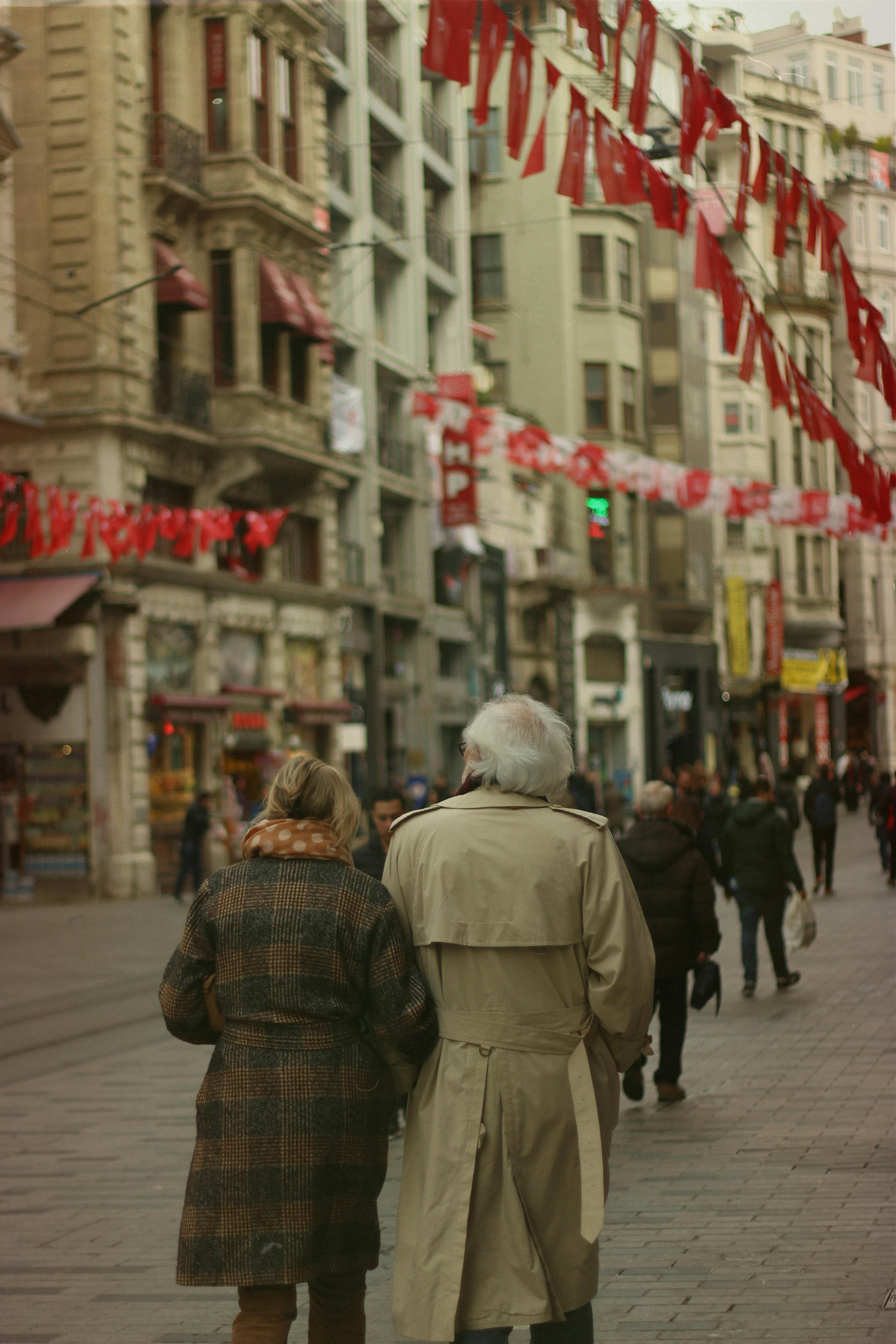 Senior couple strolling along a vibrant street adorned with red flags in Istanbul.