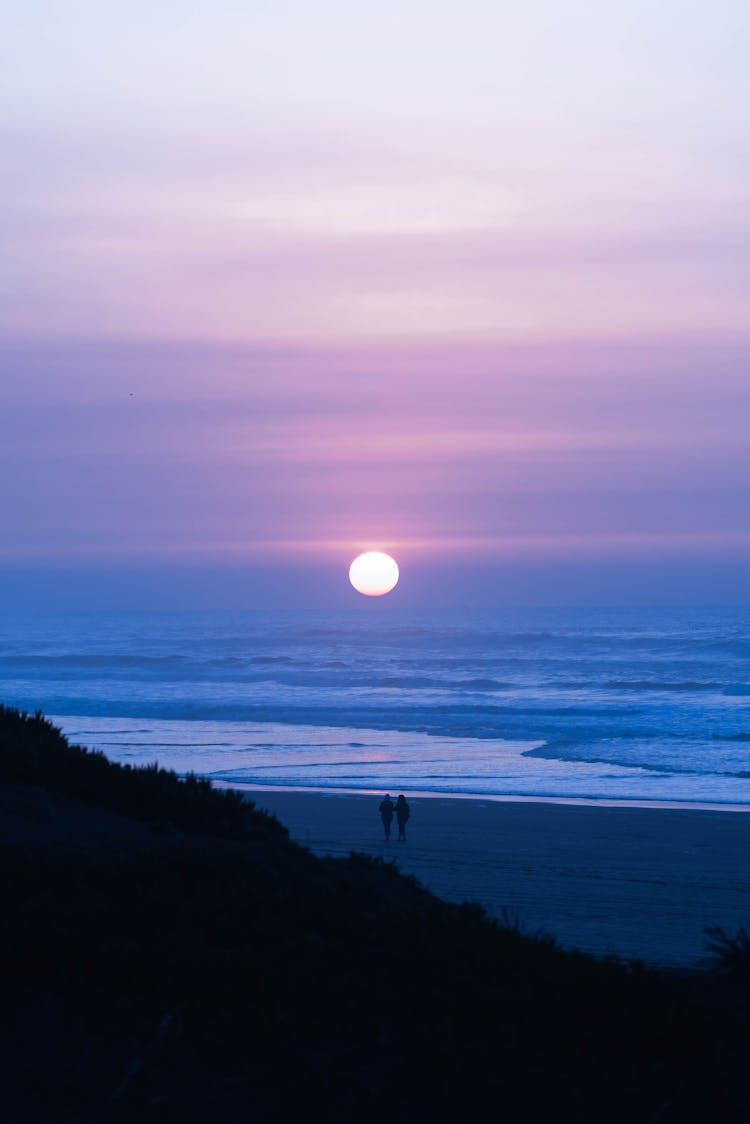 Silhouette Of A Couple Walking On Shore During Sunset