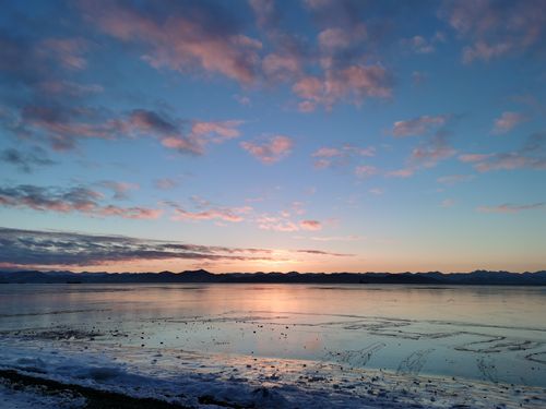 Free Breathtaking winter sunset over a frozen lake with colorful clouds and distant mountains. Stock Photo