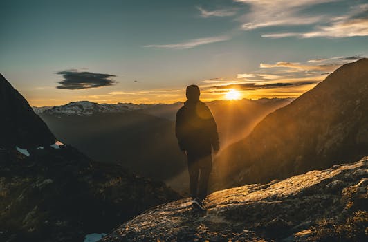A person stands on a mountain lookout during a breathtaking sunrise, showcasing nature's beauty.