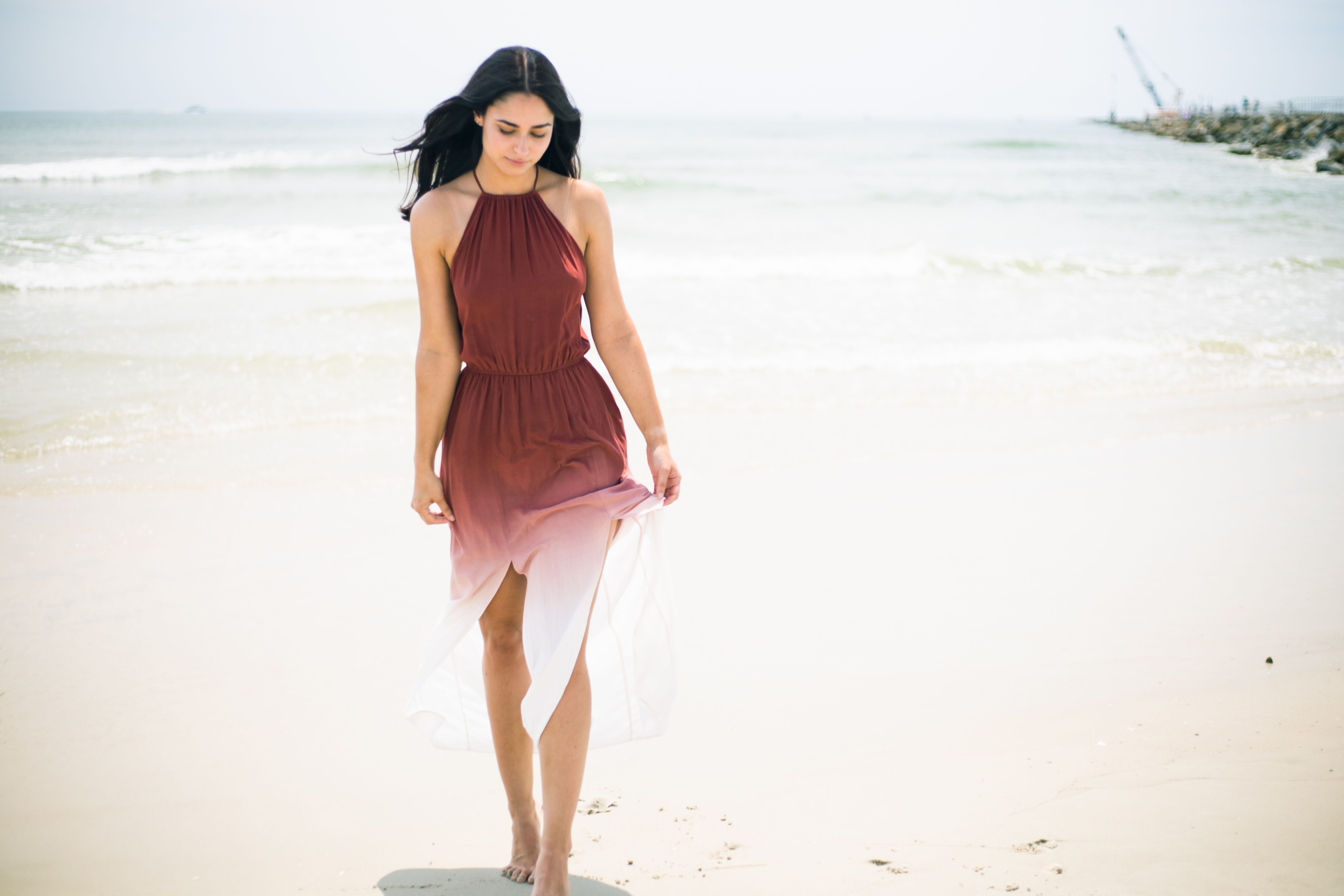 A woman in a flowing dress strolls along the sandy beach at Ponce Inlet on a sunny day.