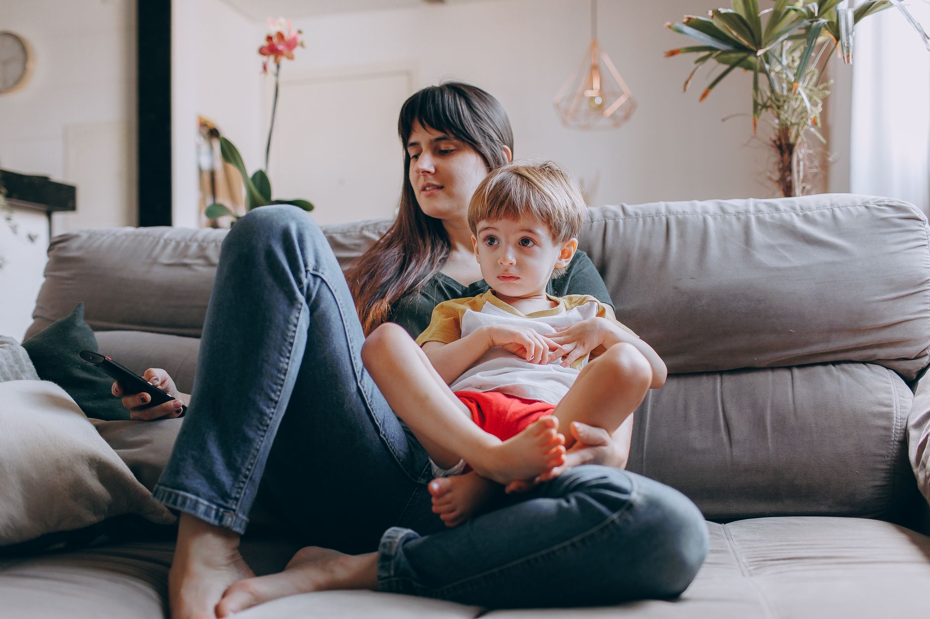 A mother and child sit close together in a bright living room, the kind of ordinary domestic scene where family scripts are learned