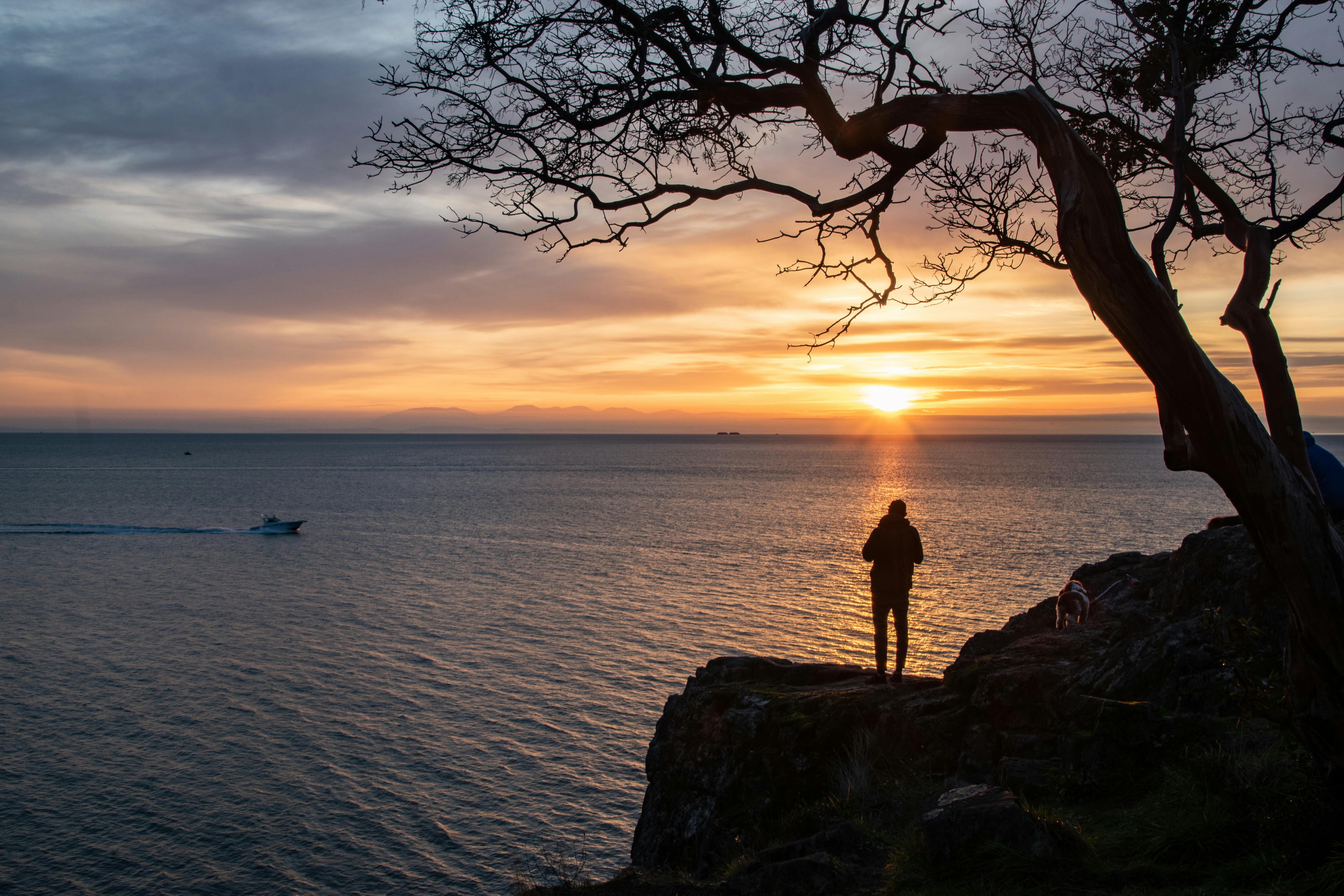 Silhouette of person enjoying a tranquil sunset over the ocean from a cliff in Vancouver.
