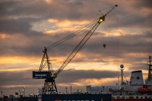 A large crane operates at a busy harbor in North Vancouver, BC during sunset.