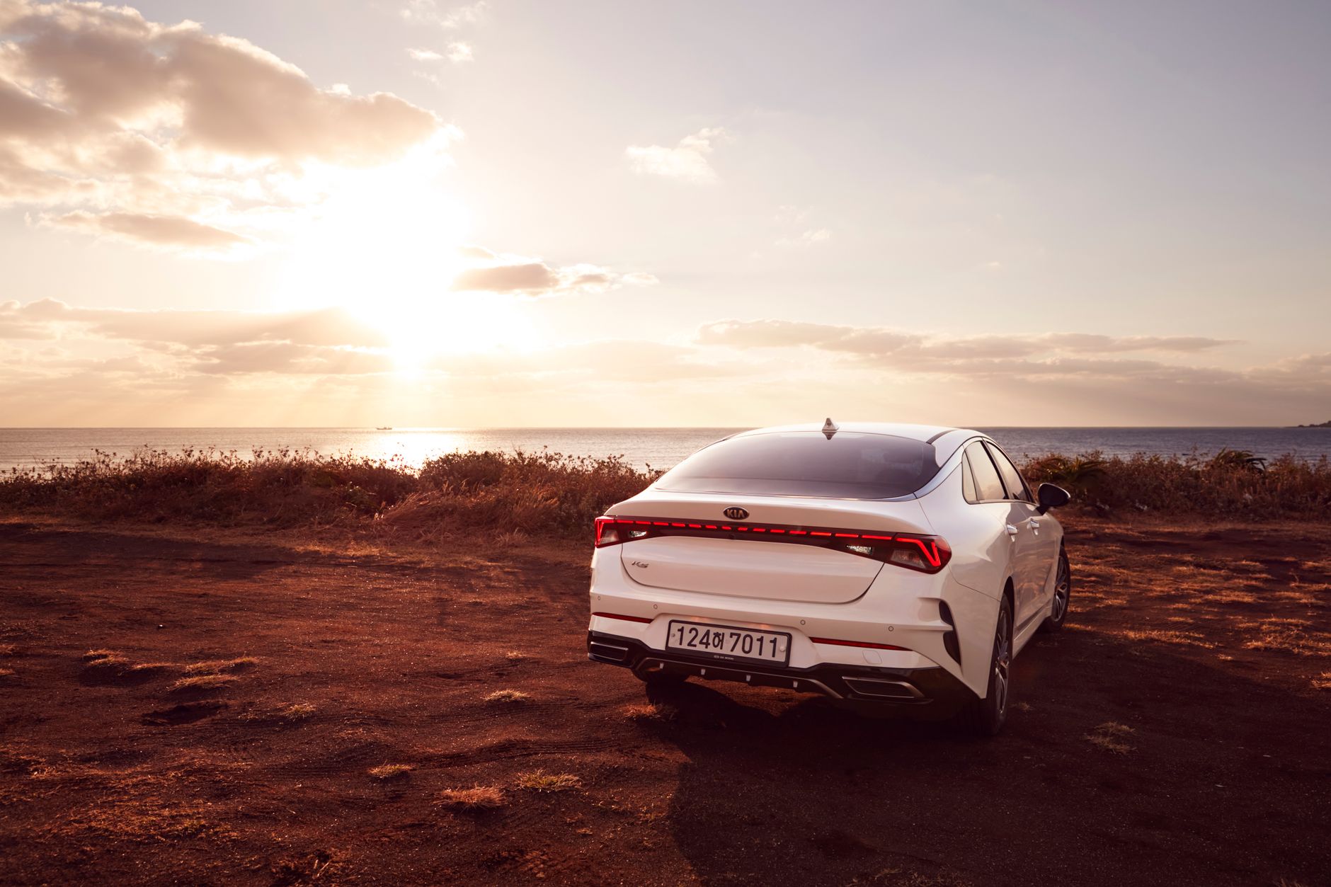A modern white car parked near the ocean during sunset, offering a serene coastal view.