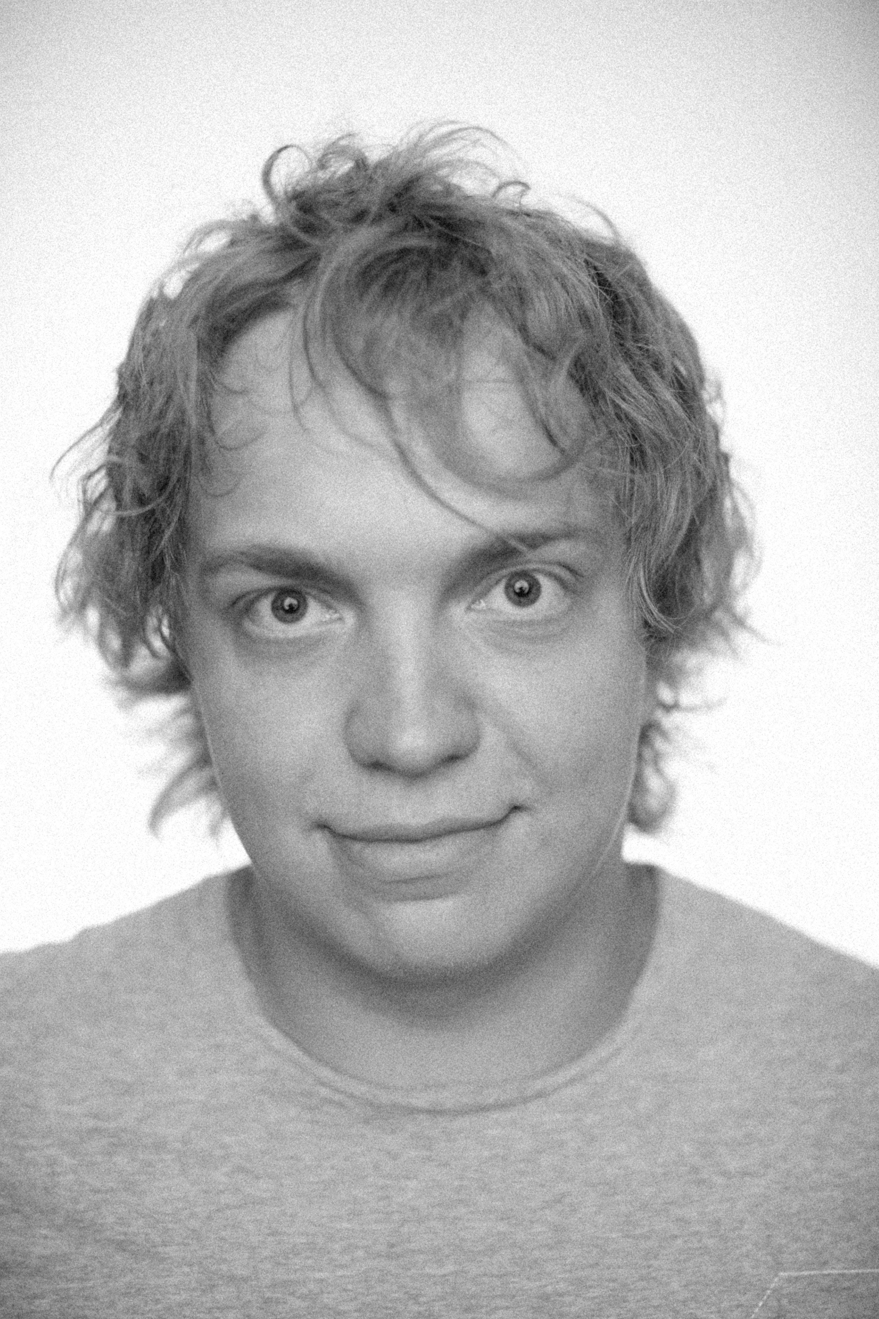 Engaging black and white portrait capturing a smiling man with curly hair in a studio setting.