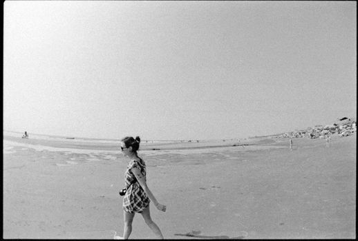 A woman walking on a sandy beach captured in classic black and white. Serene summer day.