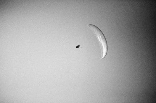 A dramatic black and white photo capturing a paraglider silhouetted against a clear sky.