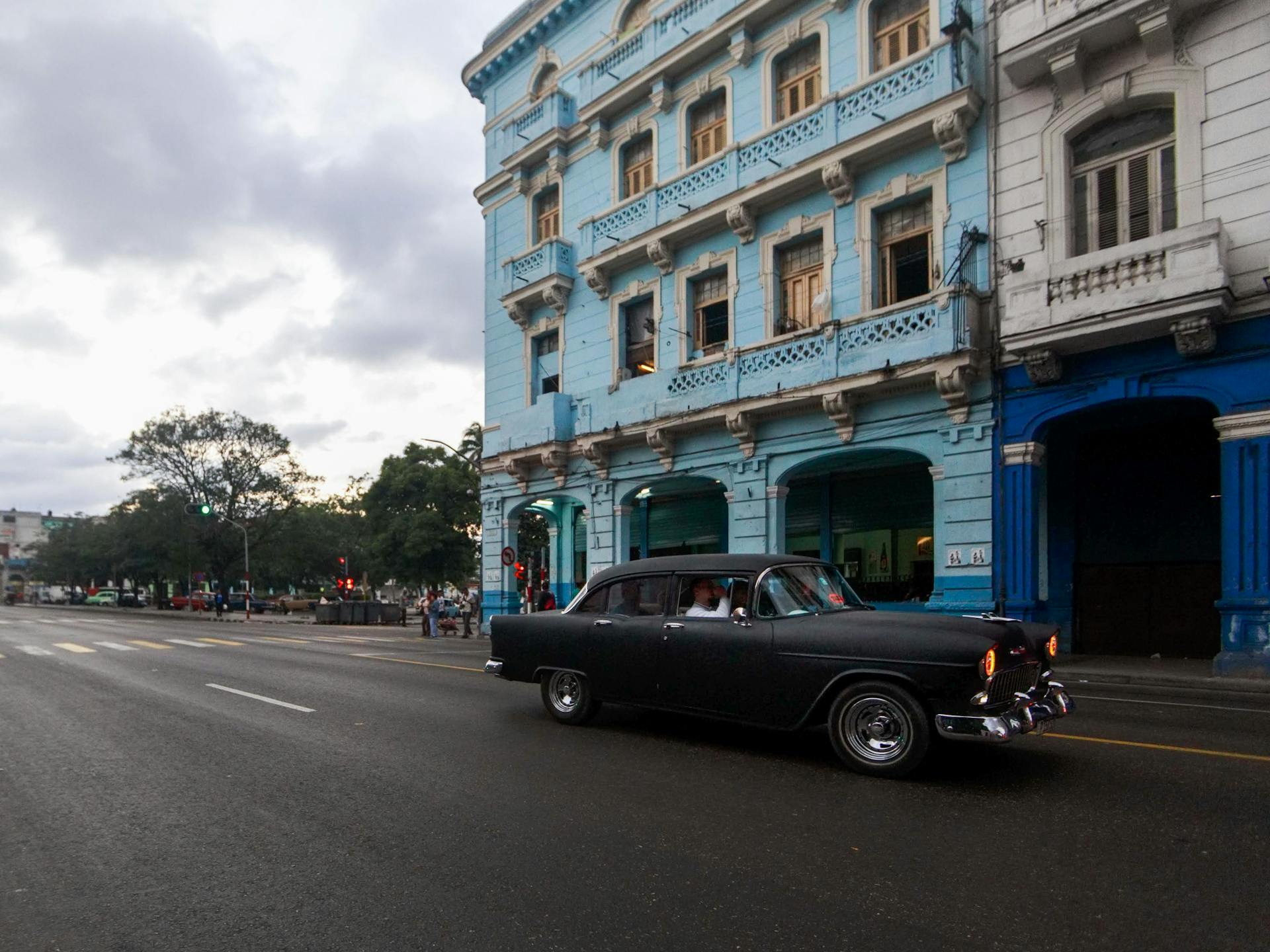 A Vintage Black Car Driving in Front of a Building