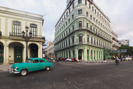 Classic green car on a vibrant urban street corner in Havana, Cuba showcasing colonial architecture.