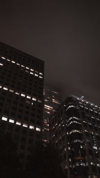 Tall high-rise buildings under a dark, moody sky at night, creating a dramatic urban scene.