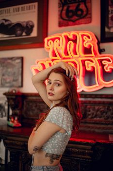 Stylish woman posing at a vintage bar in Des Moines, featuring vibrant neon sign.