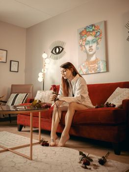 A woman sitting on a red sofa holding a rose in a stylish living room setting.
