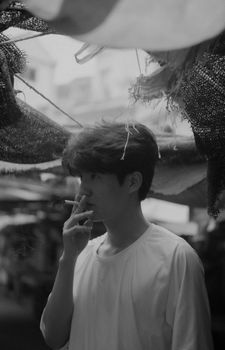 Monochrome photo of a young man smoking under canopy outdoors.