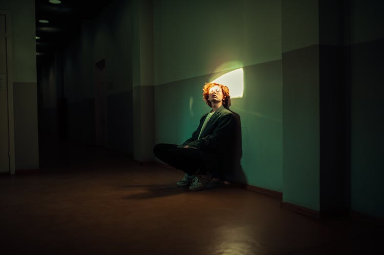 Man Sitting In Dark Room With Face Illuminated By Ray Of Light