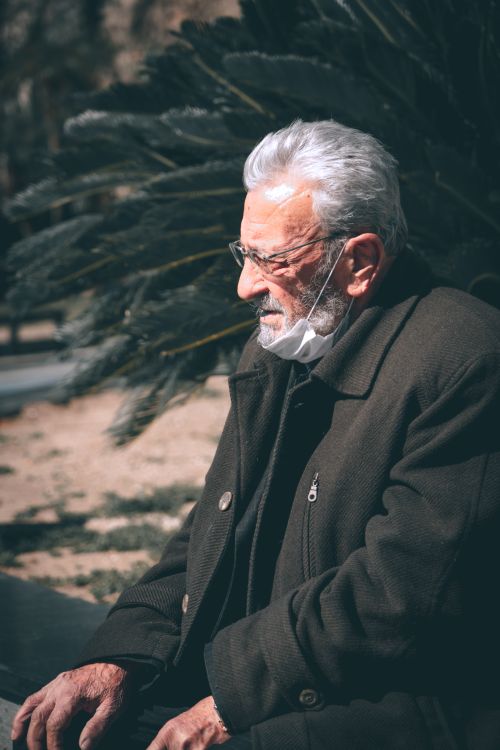 Free A senior man in glasses and coat sits outdoors in thoughtful reflection under the autumn sun. Stock Photo