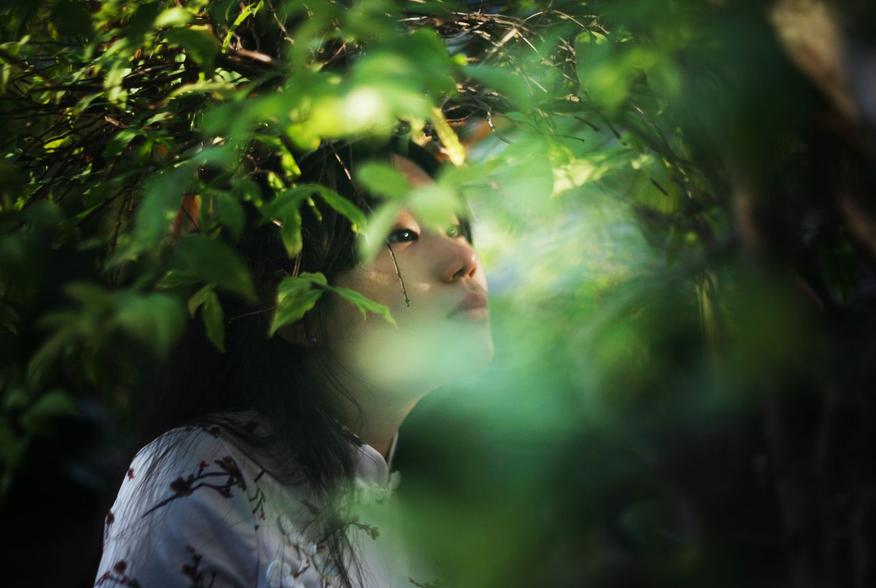 a woman gazes thoughtfully amid lush foliage surrounded by green leave