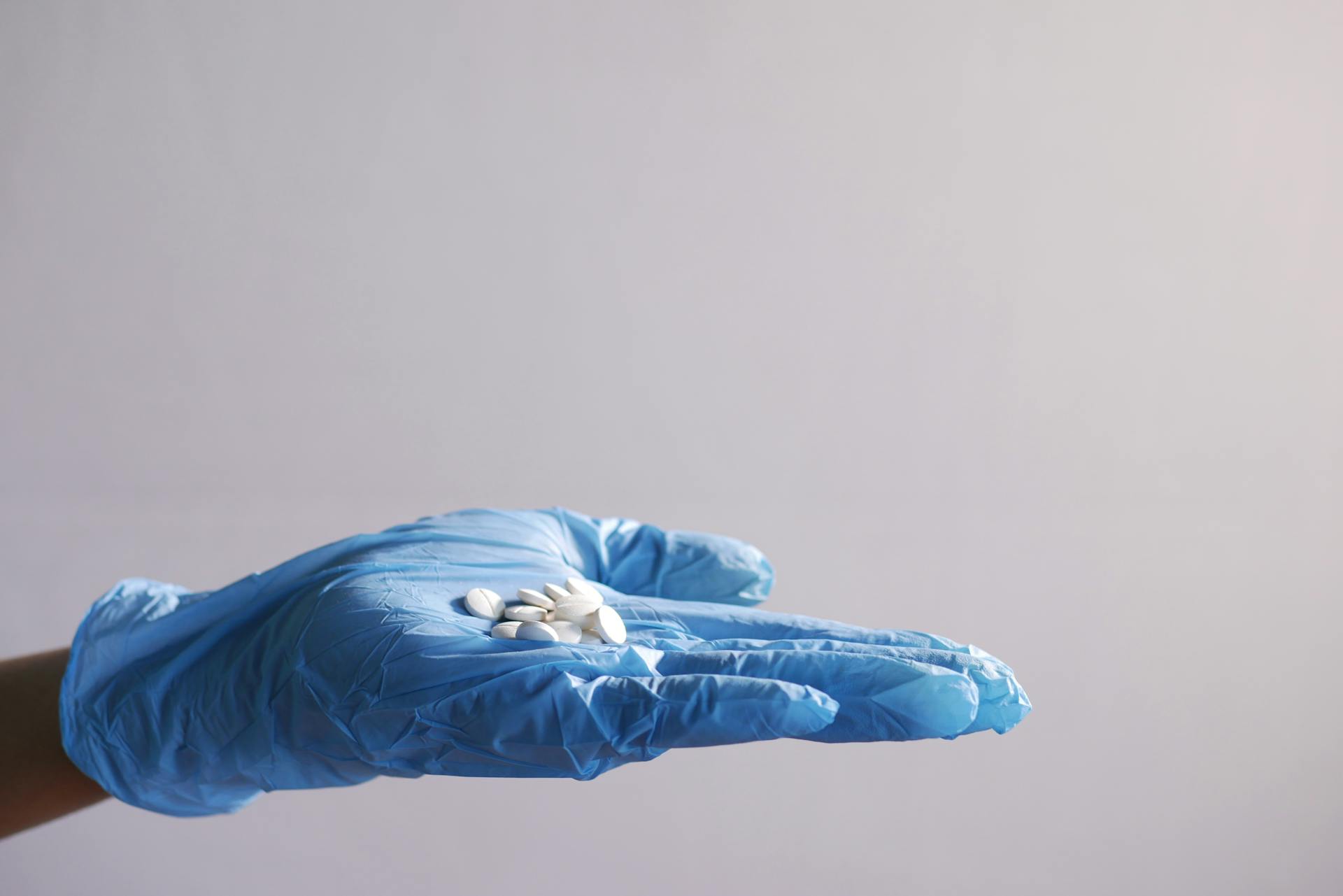 Hand in blue glove holding white pills, symbolizing healthcare and medicine.