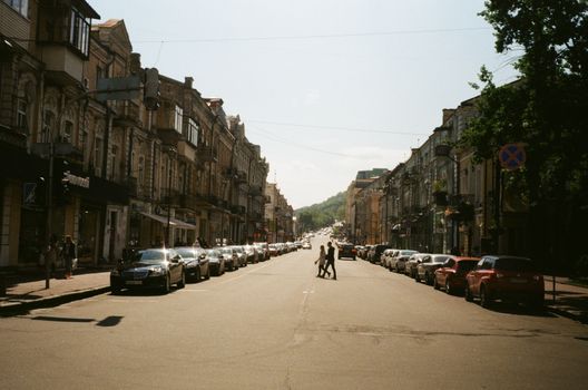 City street with historic buildings, cars parked, and people crossing.