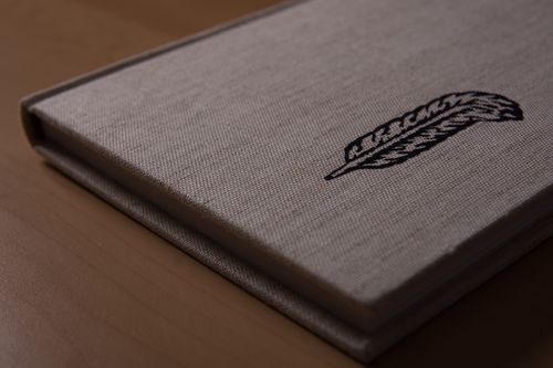 Free Book on a wooden table, with a canapa cover and a black feather printed on it Stock Photo