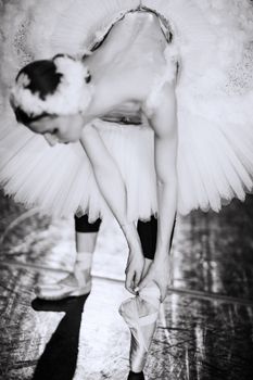 Beautiful ballerina bending down to fix her pointe shoes in a graceful black and white shot.