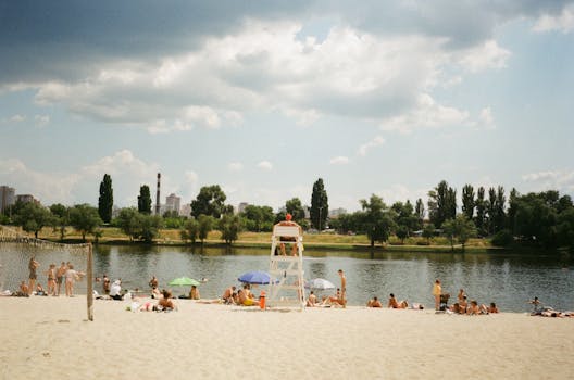 People enjoying leisure activities on a sunny riverside beach with a lifeguard present.
