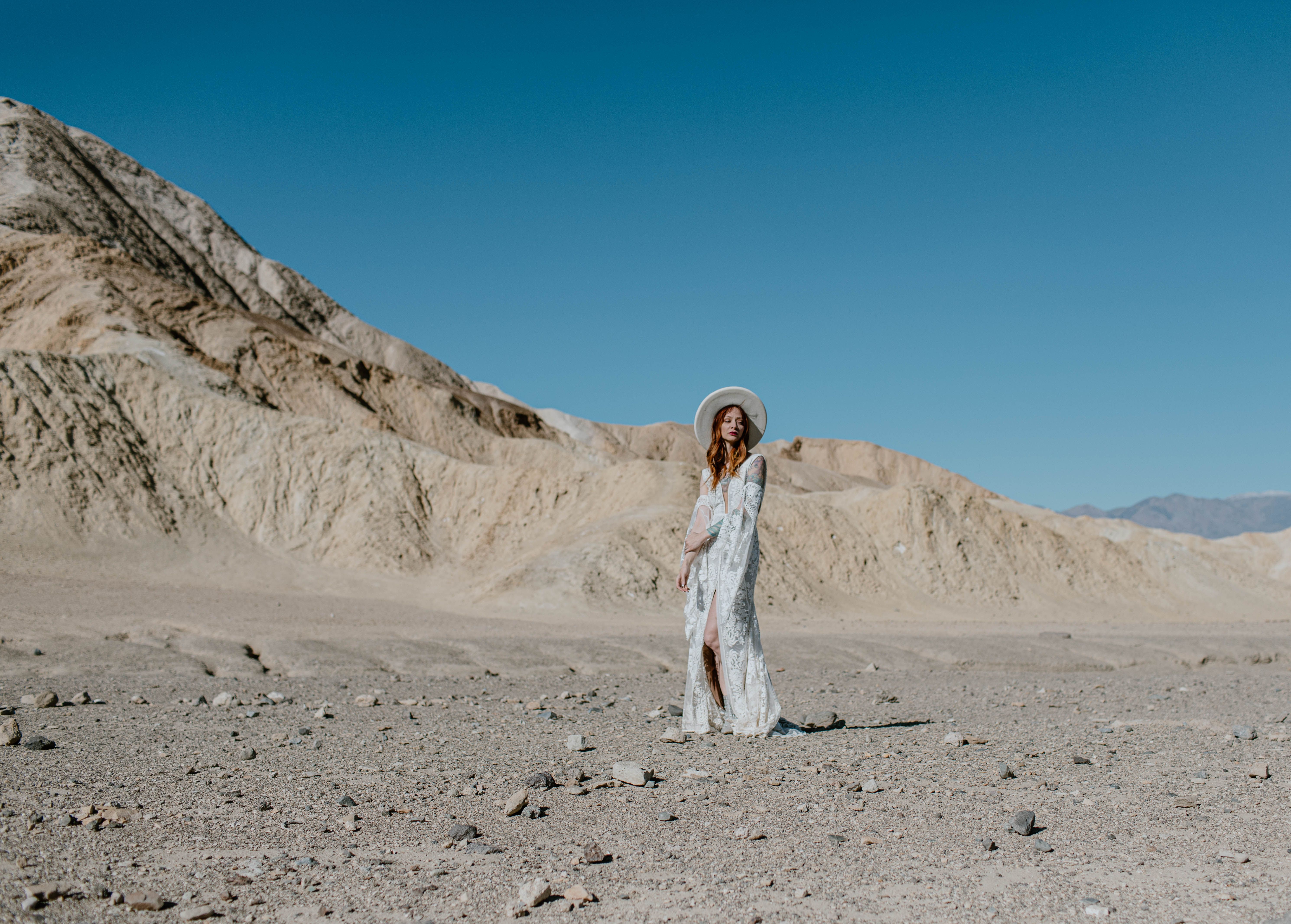Woman in bridal attire poses in Death Valley's scenic dunes under clear blue sky.