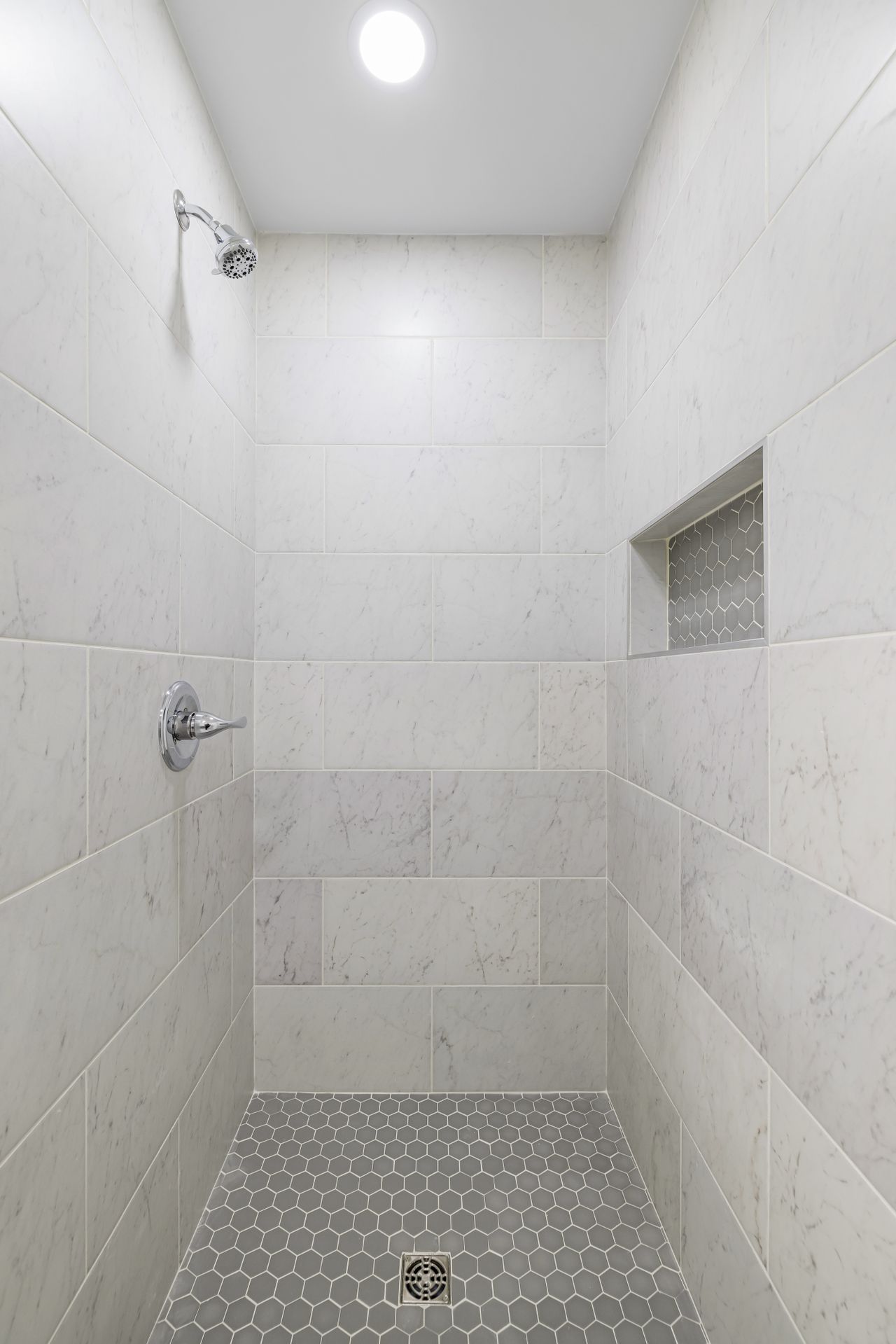 Marble-tiled walk-in shower interior with a built-in wall niche and hexagon tile floor