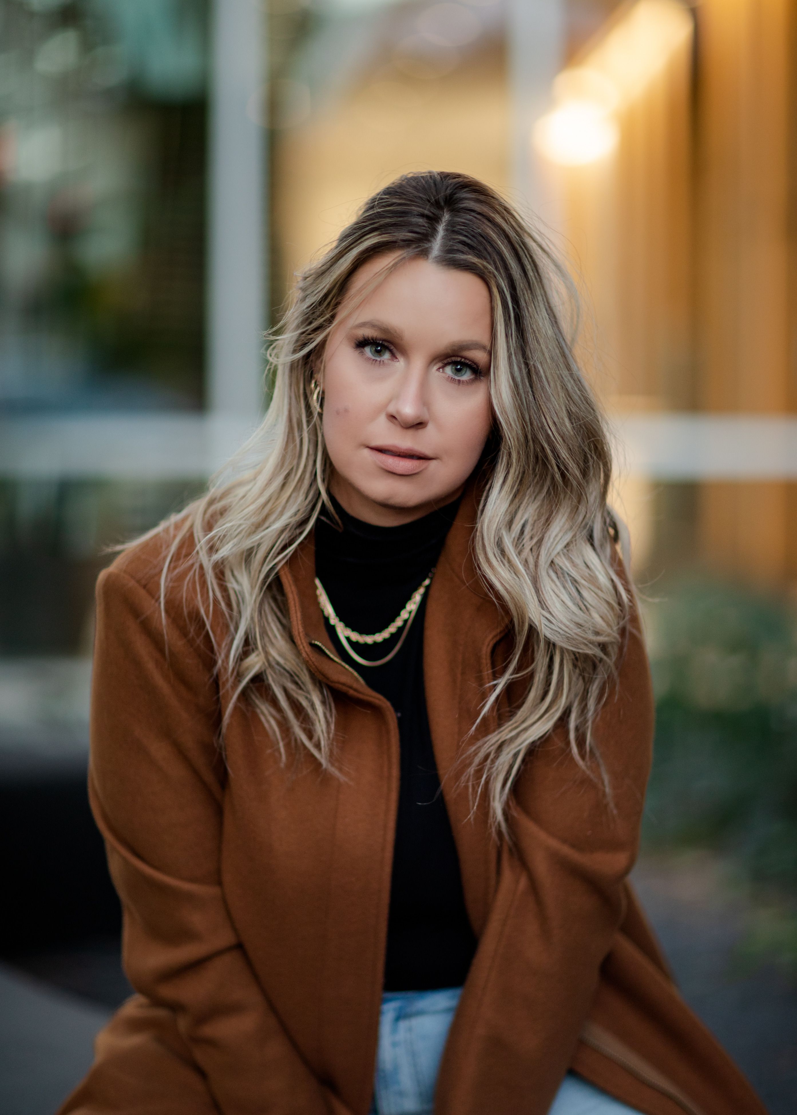 Portrait of a blonde woman in a brown coat with elegant necklaces.